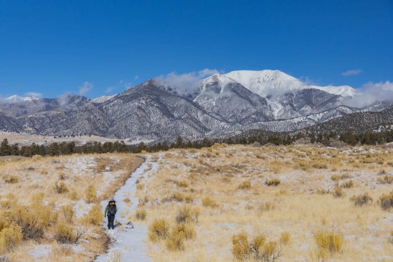 Hiker on a snowy trail headed toward mountains in Great Sand Dunes National Park.