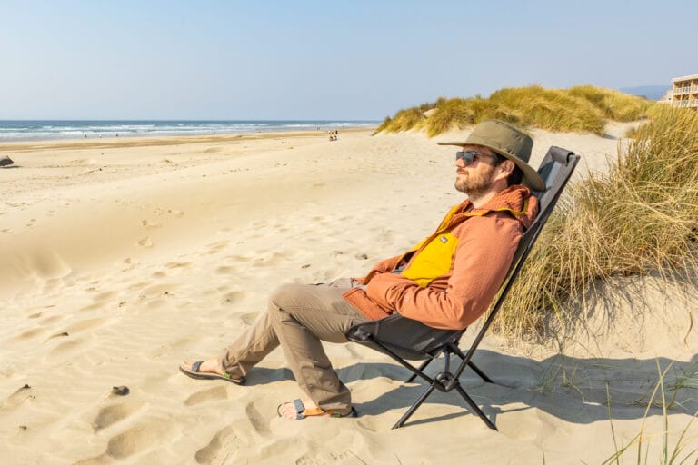 A man sits in a Helios camp chair on the beach.