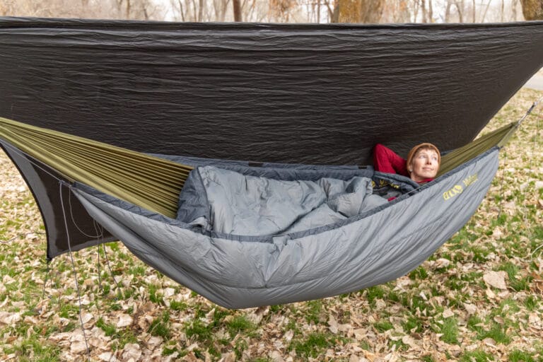 A woman relaxes in a camping hammock with underquilt and tarp.