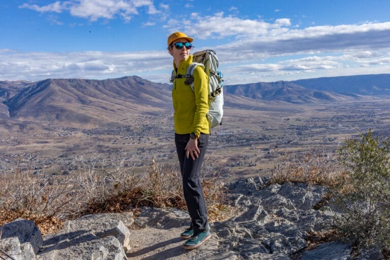 A woman stands in front of a vast valley wearing a Houdini Pace Flow 1/4 zip ultralight fleece.